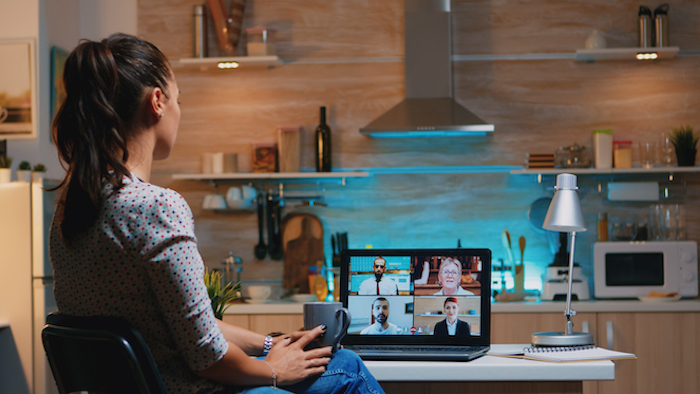 Woman zoning out at her laptop while sitting in the kitchen late at night after zooming in all day