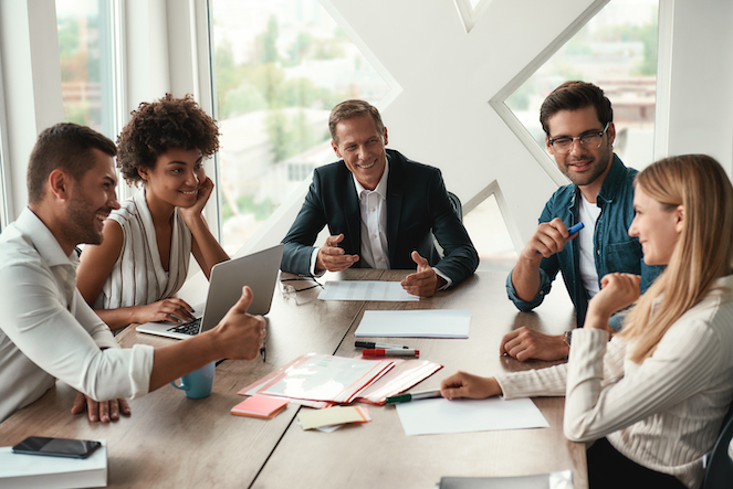 A diverse group of employees working together at a desk and smiling like they are working through a conflict. 