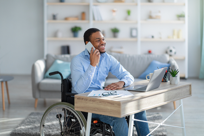 Very productive disabled employee reaching bottom lines in a wheelchair on the phone working at his desk