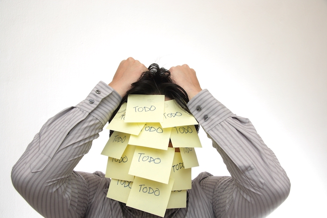 A person with todo post-it notes covering his face with his hands on his black head of hair looking stressed