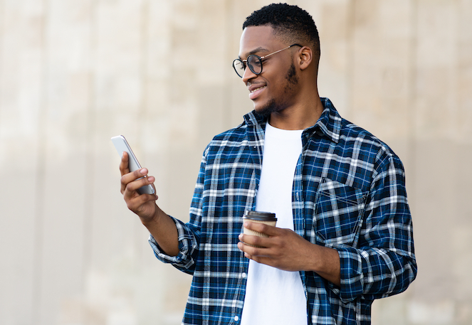 African American man with a coffee in his hand, a smile on his face while looking at a message on his phone, after being laid off