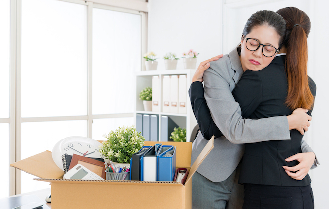 Two longtime friends and coworkers hugging after one has been laid off and has packed up her office