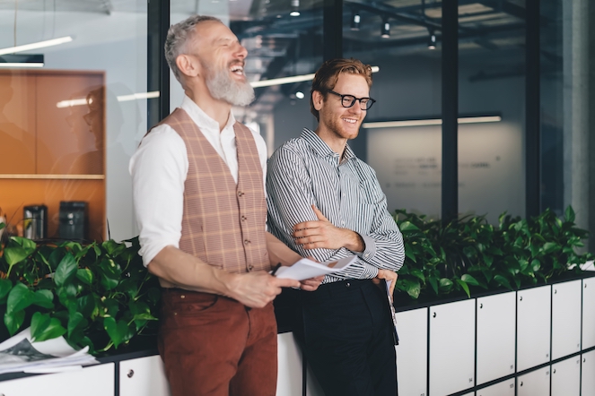 A male boss genuinely showing care for the mental wellness of his team member, both laughing at work.