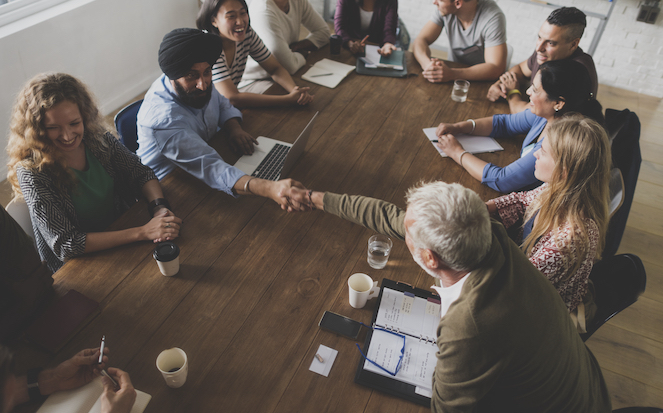 A diverse group of employees sitting around a table with coffee and water and engaged in conversations.