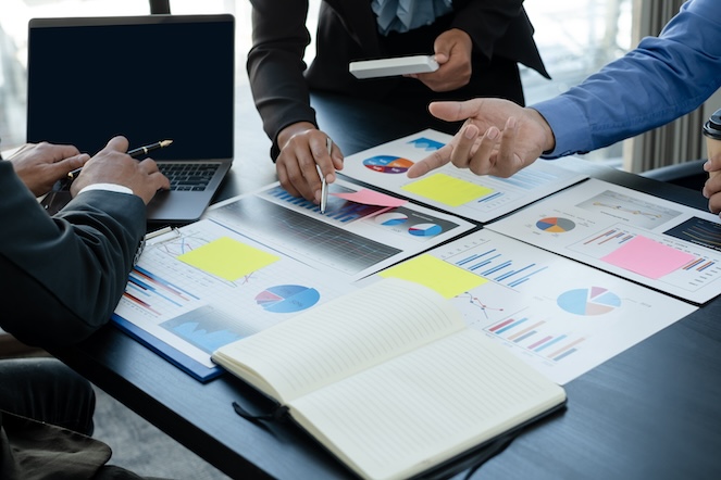 A business team measuring impact reviewing charts and graphs showing results and outcomes for the company as they work together 