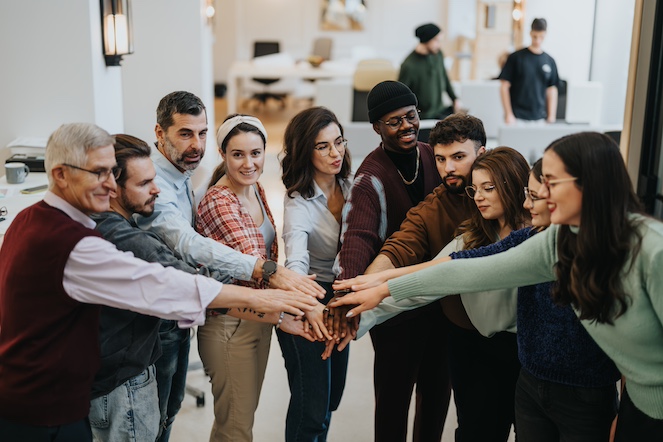 Diverse group of employees in a happy huddle in the workplace, demonstrating healthy teamwork