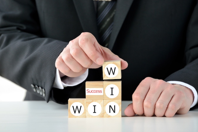 Man's hands building blocks which read win, win, and the middle block reads success. 