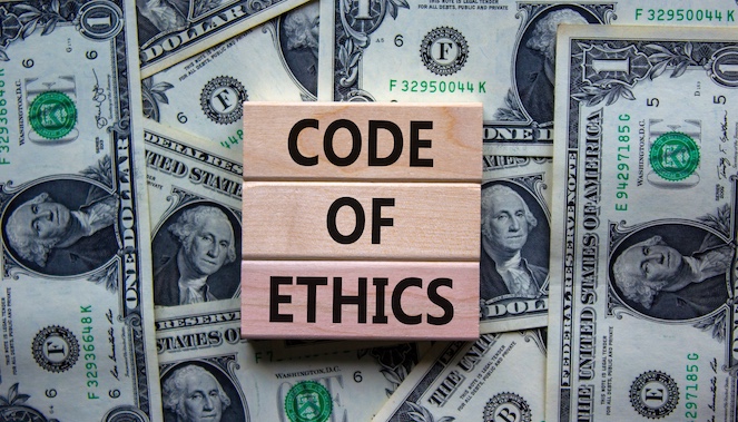 Blocks with the words code of ethics on them, sitting on a bunch of one dollar bills. 