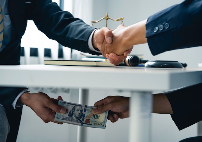 Two arms shaking hands above the table while passing money with their other hands under the table.