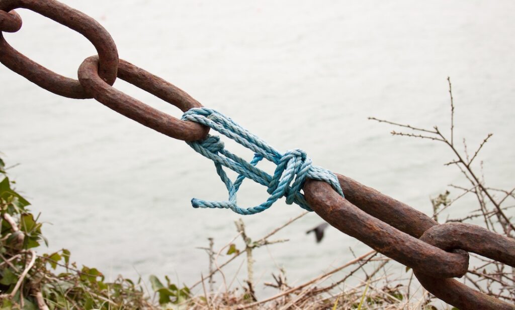 Rope repair to rusty chain, demonstrating unity despite division.