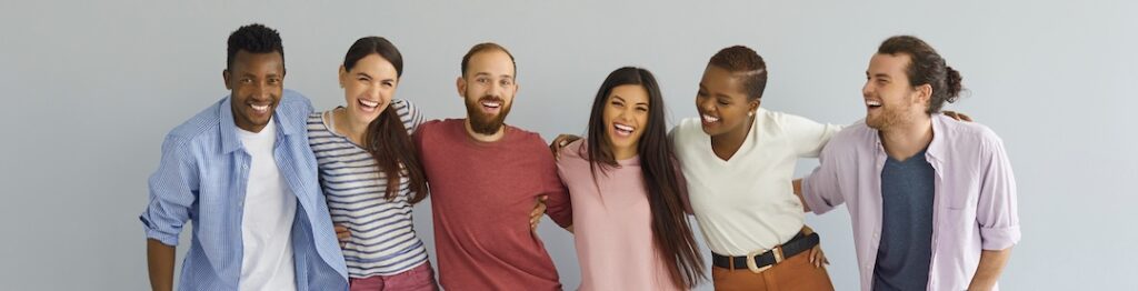 Group of close friends. Diverse team of happy cheerful sociable outgoing black and Caucasian young people in their 20s twenties in casual style clothes standing together against light grey background, demonstrating a shared purpose.
