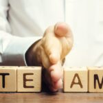 The word team spelled out in block letters with a human hand dividing right down the middle demonstrating a break in team unity.