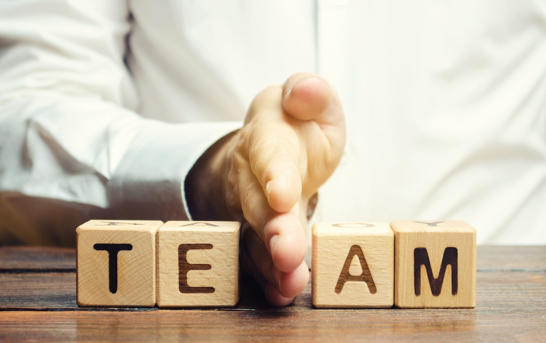 The word team spelled out in block letters with a human hand dividing right down the middle demonstrating a break in team unity.