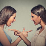 Two angry women pointing fingers at each other.