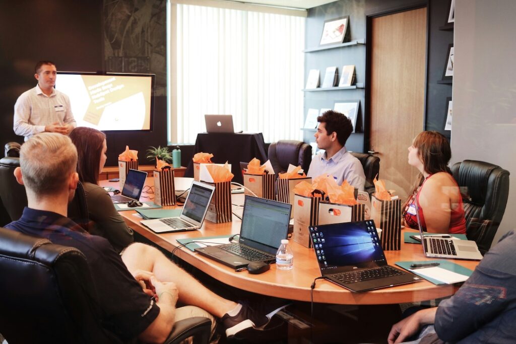 A group of people sitting at a table with their laptops open and listening to a presentation.