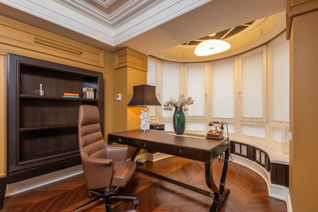 Beautiful corner office with a wooden desk and wooden shelves facing the windows.