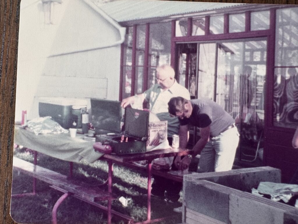 Two men making a backyard meal in the summer time with an indoor pool in the background