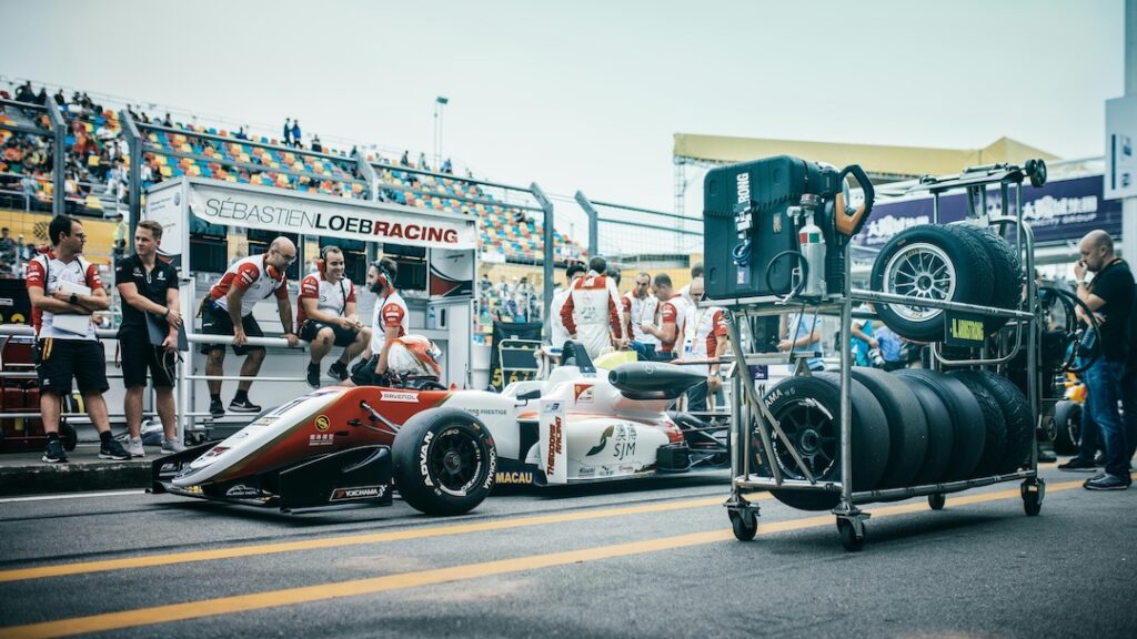 Race car and crew at the pitstop on the course with the driver in the seat. 